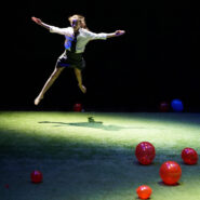 A girl in school uniform leaps into the air from green turf