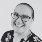 Smiling person wearing glasses and a floral top in a black-and-white portrait; conveys a joyful and friendly tone.