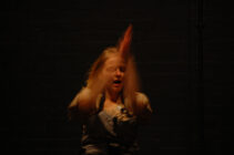 A person in motion with blurred arms claps in dim lighting against a dark background, conveying energy and intensity.