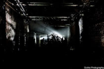 A dark, industrial setting with silhouetted figures arranging a spotlighted art installation, casting dramatic shadows. Edgy and mysterious atmosphere.