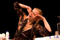 A woman in a floral robe poses playfully with animated facial expressions. A carton of milk is on the table in a dimly lit setting, evoking a whimsical tone.