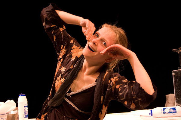 A woman in a floral robe poses playfully with animated facial expressions. A carton of milk is on the table in a dimly lit setting, evoking a whimsical tone.