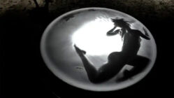 Silhouette of a person underwater, backlit by bright light, creating a circular window effect. The scene conveys a sense of mystery and serenity.