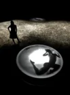 Silhouette of a woman standing on a textured surface, looking at a large lit circular platform. A floating, shadowy figure is visible inside it, creating a mysterious, contemplative mood.