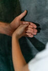 A child's hand gently holds an adult's hand, both against a dark textured background. The image conveys warmth, care, and protection.