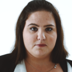 Portrait of a woman with medium-length brown hair, wearing a black jacket. She has a neutral expression, against a plain white background.