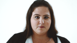 Portrait of a woman with medium-length brown hair, wearing a black jacket. She has a neutral expression, against a plain white background.