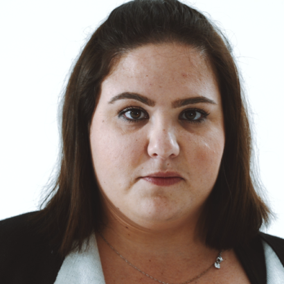 Portrait of a woman with medium-length brown hair, wearing a black jacket. She has a neutral expression, against a plain white background.