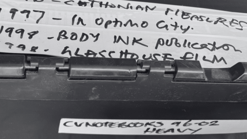 Close-up of a labeled black storage container, noting events from 1996 to 1998, including publications and a film title.