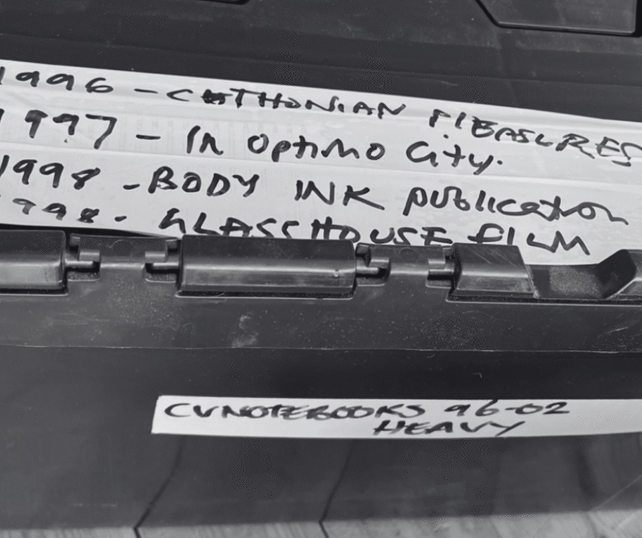 Close-up of a labeled black storage container, noting events from 1996 to 1998, including publications and a film title.