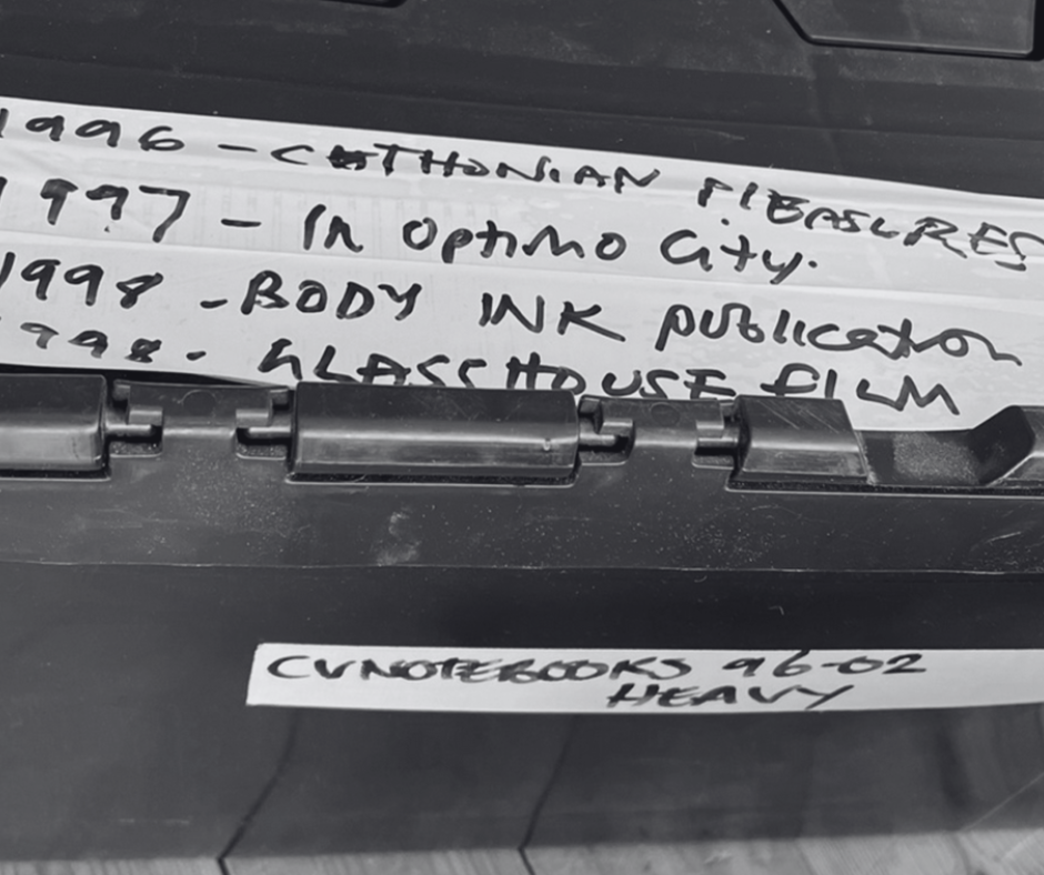 Close-up of a labeled black storage container, noting events from 1996 to 1998, including publications and a film title.